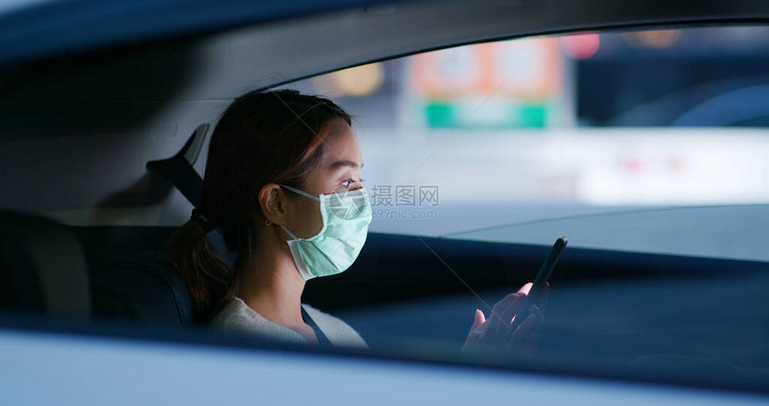 妇女戴医疗面罩使用手机坐在车内图片