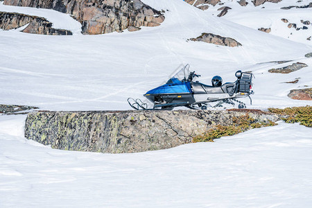 阿托克林滕一辆蓝色雪地摩托站在靠近挪威山脉石头的雪地上背景
