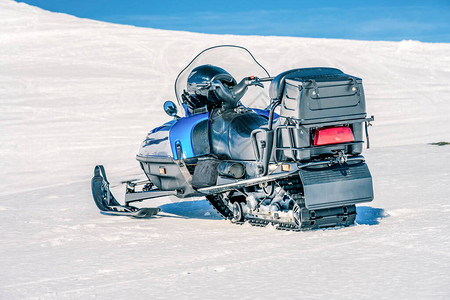 一辆蓝色雪地摩托站在挪威山坡上的地壳雪上图片