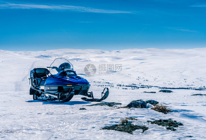 一辆蓝色的雪地摩托站在挪威山区的地壳雪上图片