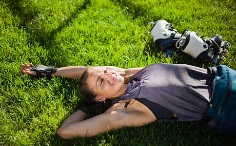 年轻快乐的运动女子轮滑运动员躺在公园的草坪上休息图片