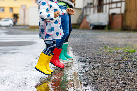 三个孩子蹒跚学步的女孩和两个男孩穿着红色黄色和绿色雨靴图片