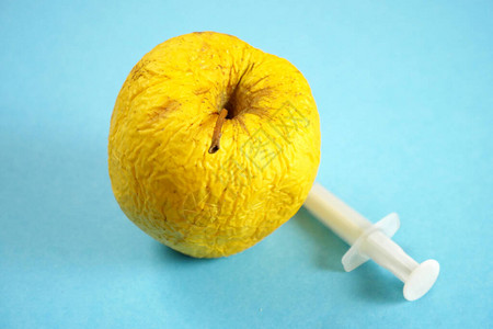 带有注射器的转基因黄苹果在蓝色背景上实验室概念中带注射器的图片