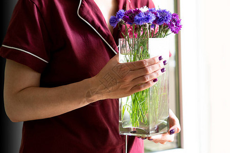 一个穿着栗色西装留着紫色指甲的女人拿着一瓶矢车菊送花服务在图片