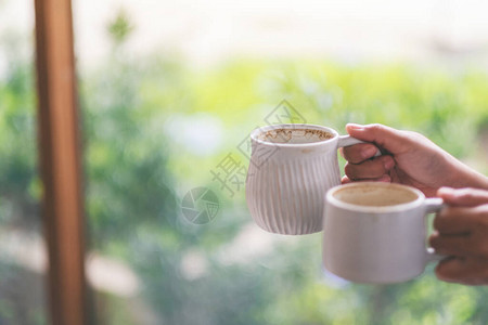 握着两杯白色咖啡热咖啡的双手和模糊自然背景图片