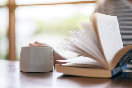 一位女子在木制桌上喝咖啡时持有和阅读一本图片