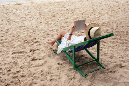 一个美丽的女人躺下躺在沙滩椅子上读书感图片