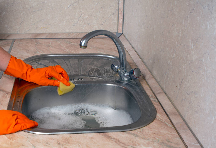 一位穿橙色橡胶家庭手套的清洁女工用黄色海绵洗一个水槽图片