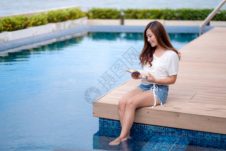 一个美丽的亚洲女人在游泳池边看书轻图片