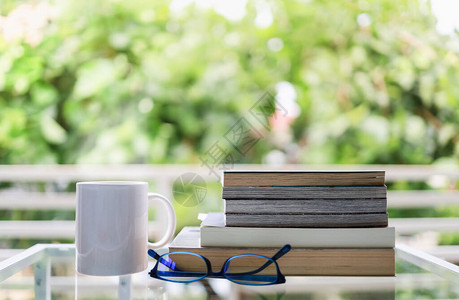 教育和放松的概念绿色花园景观玻璃桌上白杯热咖啡阅读眼镜图片