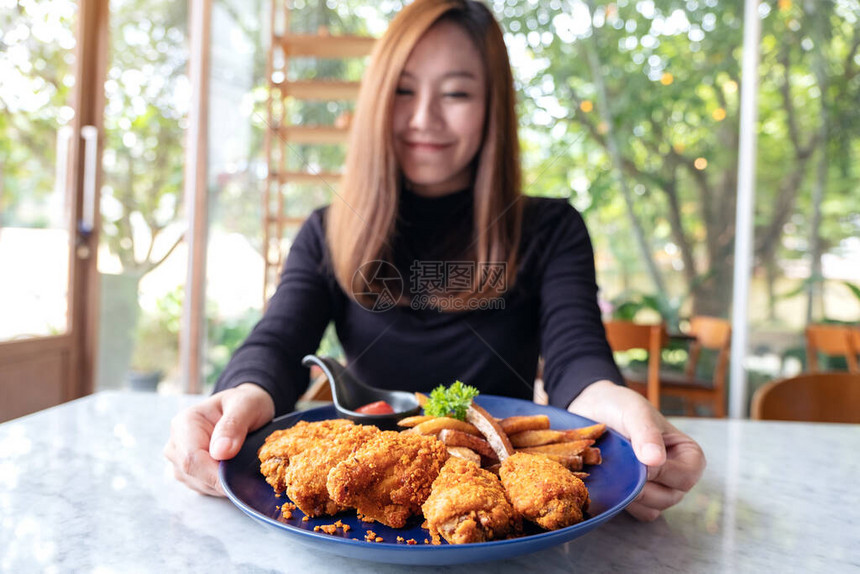 一位美丽的亚洲女在餐厅里拿着并展示一盘炸鸡和薯条的近视画面图片