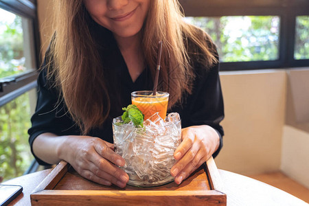 一个女人在一罐冰里拿着一杯橙子和胡萝卜汁的混合杯子图片