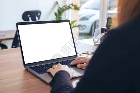 一名妇女用笔记本电脑并在办公室木制桌子上空白桌面屏幕使用和打图片