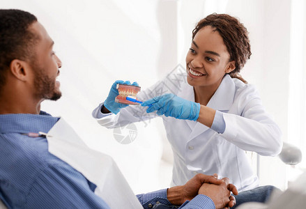 牙医微笑的非洲女向耐心的年轻人展示图片
