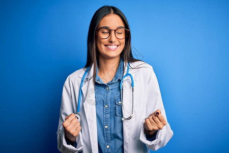 年轻漂亮的医生女人戴着听诊器和蓝色背景的眼镜图片