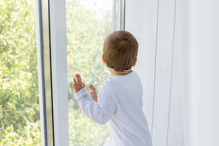 一个两岁小男孩的背影站在窗边等待着一些东西图片