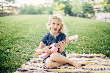 可爱的金发女孩在户外玩粉红色的吉他玩具孩子在公园里演奏音乐和唱歌孩子们的爱好活动温柔难忘的真实坦背景图片