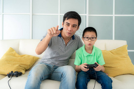 亚洲家庭父亲教他的儿子坐在家里客厅的沙发上玩电子游戏图片