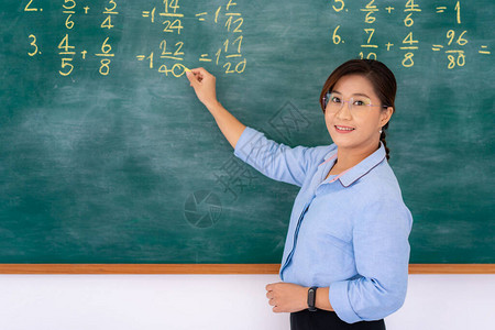 亚洲小学教师在黑板上解释数学背景图片