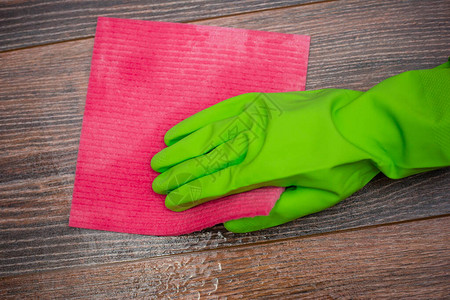 一只手在绿色橡胶手套中摩擦湿木表面的特写图片