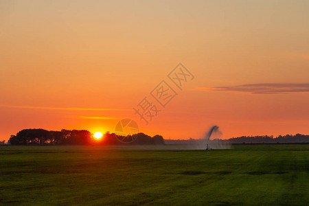 农民灌溉他的土地和太阳落日图片