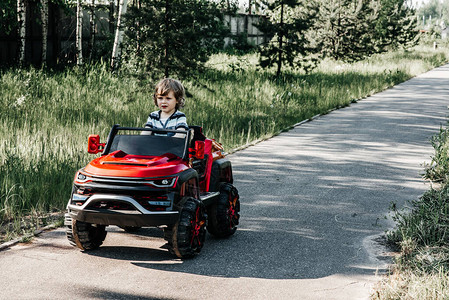 穿条纹T恤衫的卷发男孩骑着一辆红色大玩具车在沥青路上行驶背景图片
