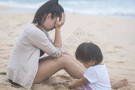 母亲当女儿在沙滩上玩耍时她正在强调图片