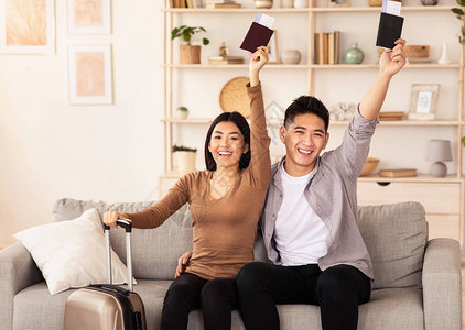 准备渡假亚洲配偶带着票欢乐的手举起手来讨论在家沙发上的图片