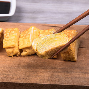 木板上的日本玉冈煎蛋卷筷子拿着一块煎高清图片