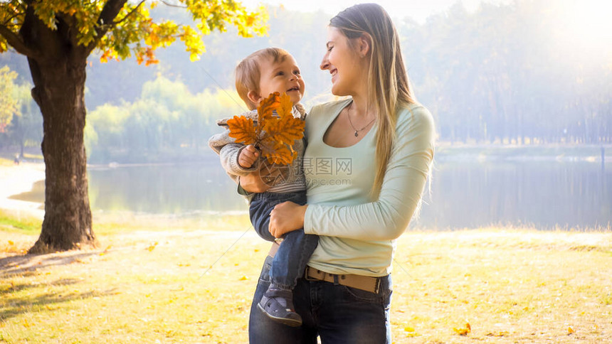 在秋天公园拥抱她的小儿子充满了快乐微笑的年图片