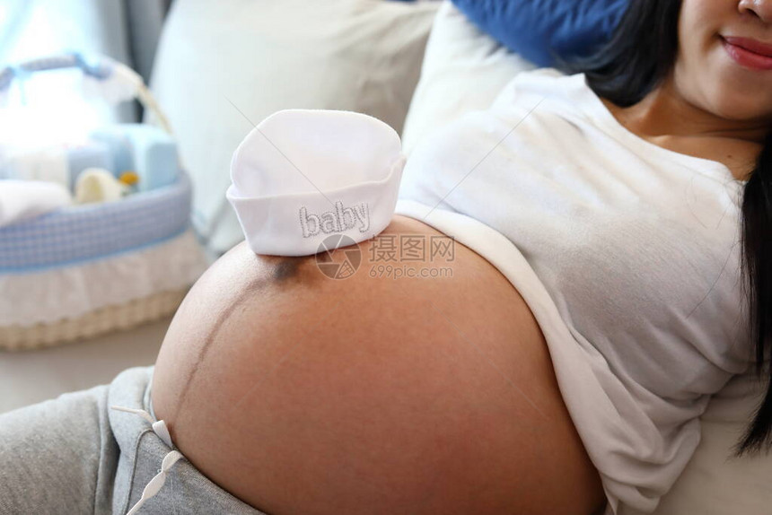 戴上可爱的婴儿帽子在等待新生儿的孕妇肚图片