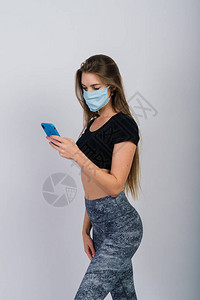 长发女孩用外科面罩看智能手机和锻炼身体图片