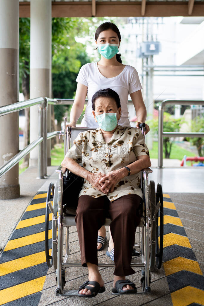 年轻的亚洲孙子照顾她坐在轮椅上的祖母近90岁的祖母在公园旅行时由孙女照顾戴着图片