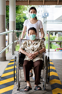 由远及近年轻的亚洲孙子照顾她坐在轮椅上的祖母近90岁的祖母在公园旅行时由孙女照顾戴着背景
