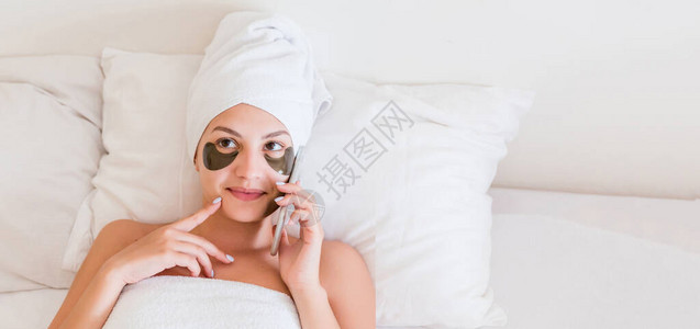 洗完澡后用毛巾包着的年轻女和眼睛下的斑点正在床上放松图片