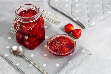 新鲜草莓旁边的玻璃罐中的草莓酱在灰色的背景上自制冬季水果空白选择焦图片
