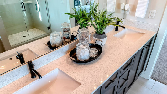 全景瓷砖地板橱柜上方的白色台面上带黑色水龙头的两个水槽浴室内还可以看到托盘罐子植物镜子背景图片