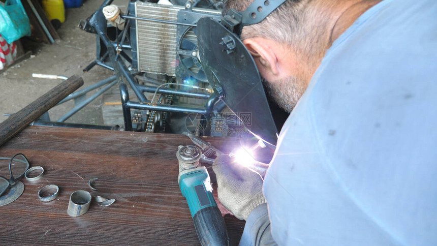 无法辨认的焊工在车库或车间焊接金属零件机械师使用焊接机进行工作和保护面罩免受闪光图片