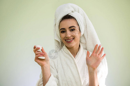 淋浴后穿着浴袍和毛巾的美丽年轻女子在晚上涂奶油面膜美丽背景图片