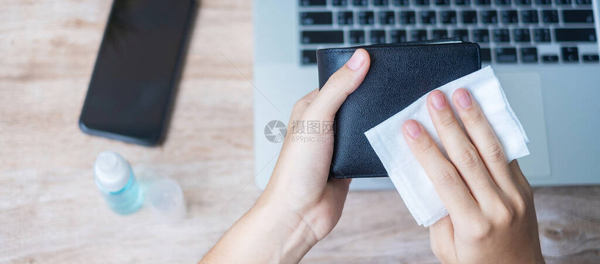 妇女在家工作时用湿巾纸和酒精消毒剂在工作场所清洁钱夹和小工具图片