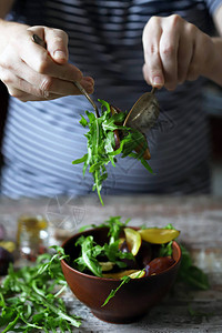 男手用勺子和叉子在碗里混合沙拉清淡的沙拉配芝麻菜和李子秋天的李子沙图片