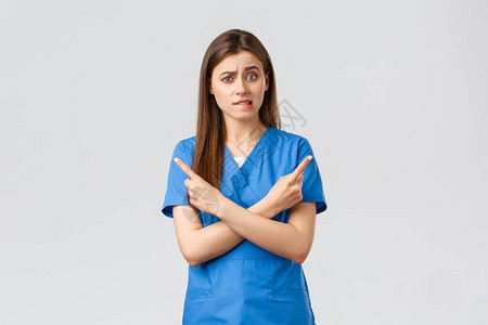 犹豫不决和困惑的女护士蓝洗涤剂医生在横幅上指向侧面图片