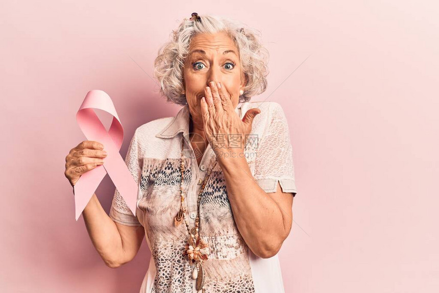 穿着粉红色癌症丝带的白头发高龄妇女用手遮住嘴部图片