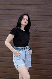 身穿黑色T恤和棕墙背景的牛仔短裤的美丽有吸引力的黑发美女背景图片