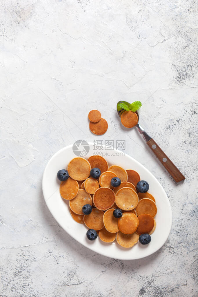 特伦迪自制早餐煎饼麦片以白混凝土和勺子及蓝莓为背景的白色盘子上小薄饼图片