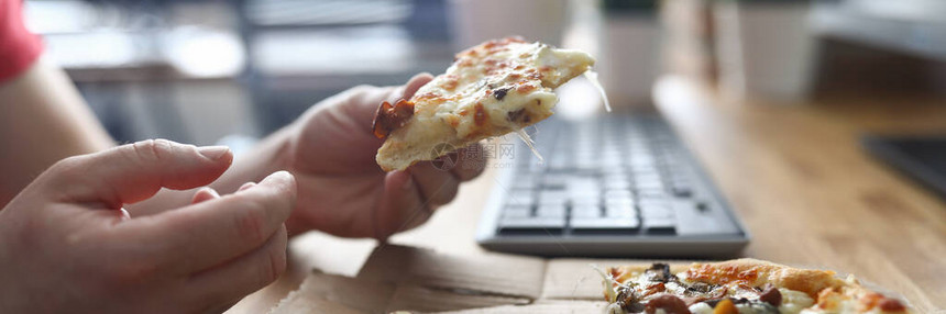 在工作场所在电脑前吃披萨的人特写手拿切片披萨订购比萨饼送货到办公室午餐时间的快餐饥饿图片