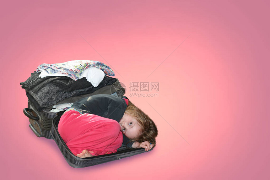 一个孩子躺在一个折叠着东西的手提箱里旅行的概念和东西和衣服的造型在粉图片