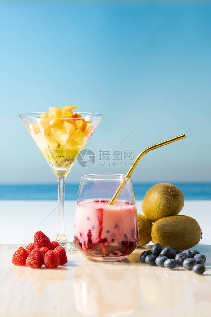 周围环绕着蓝莓猕猴桃覆盆子和一杯装满杏菠萝和猕猴桃的马提尼酒杯图片