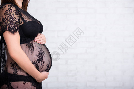 孕妇在白砖墙背景下抚摸腹部的特写镜头图片