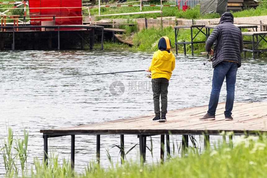 父亲教他的儿子钓鱼父亲节的概念穿着黄色夹克的图片